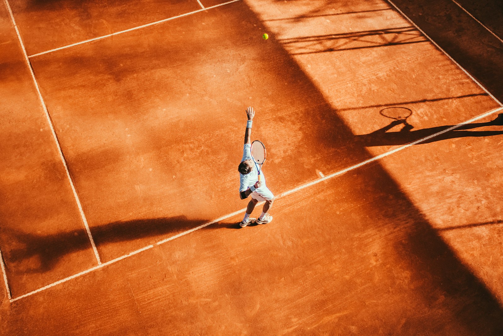 Player serving on a warm clay court, seen from above